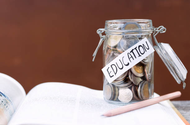 istock Open textbook, pencil, and coins in a glass bottle on the table. 940143536