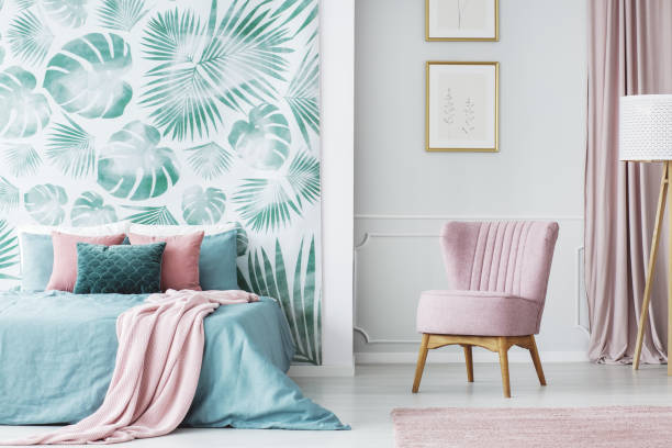Comfortable pale pink upholstered chair Comfortable pale pink upholstered chair in a cozy bedroom interior with double bed and green and leaves decorations bed decoration stock pictures, royalty-free photos & images