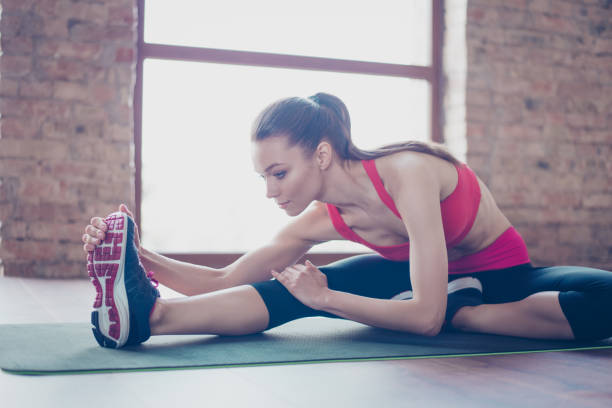 istock Focused young lady is doing her stretching to be bendy and flexible. She is wearing pink sportswear and stylish sneakers 940157076