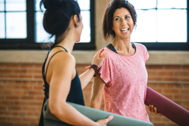 due donne che parlano e ridono. preparazione della lezione di allenamento yoga - friendship women exercising gym foto e immagini stock