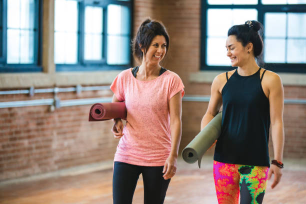 istock Two smiling women carrying an exercise mat and getting ready for a yoga class 940159690