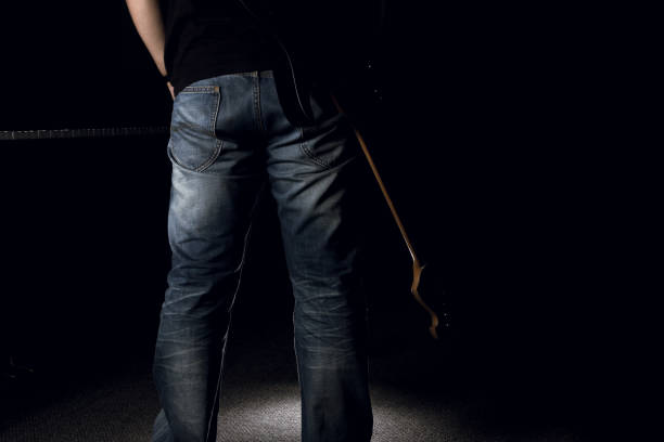 A man in jeans holding his electric guitar on black background stock photo