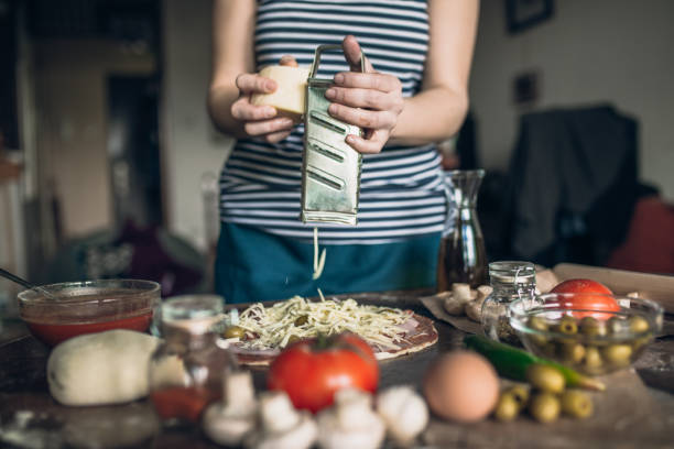 Young woman making pizza in domestic kitchen at home, with traditional pizza ingredients