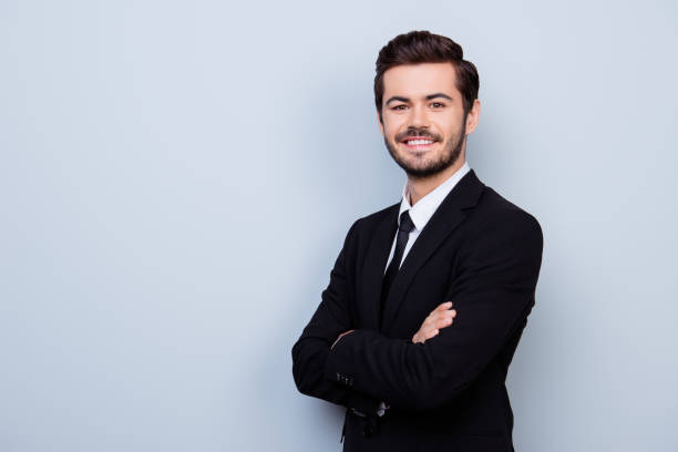 istock Happy smiling young handsome guy in formal wear with crossed hands standing half-turned against gray background 940178014
