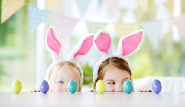 istock Two cute little sisters wearing bunny ears playing egg hunt on Easter 940182612