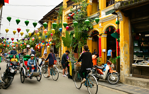 Hoi An, Vietnam - December 22nd 2017. Tourists walk, cycle or are driven by cyclo drivers down a street in the historic UNESCO listed Vietnamese town of Hoi An.