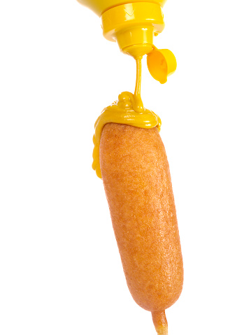 Corn Batter Crusted Hot Dog with Mustard pouring from above.