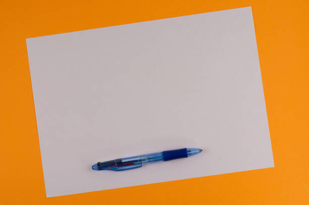 istock One multi color blue transparent ballpoint and white blank rectangle paper on background of orange paper with copy space 940223516