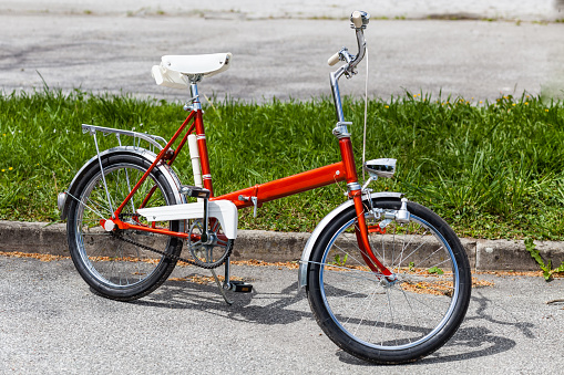 Vintage classic 1970s red folding bicycle bike in perfect condition parking on the road near grass