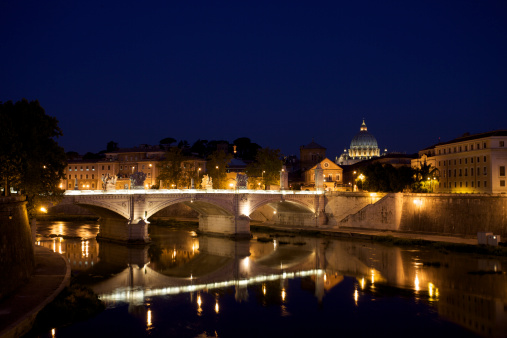 Bridge reflected in the Tiber river and St. Peter's Basilica on background. Rome, Italy