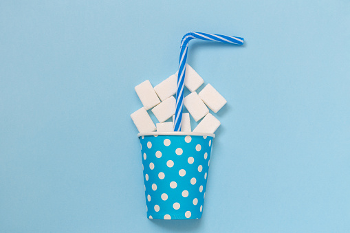 Flat lay of paper cup polka design full of sugar cubes and drinking straw against pastel blue background minimal creative concept.