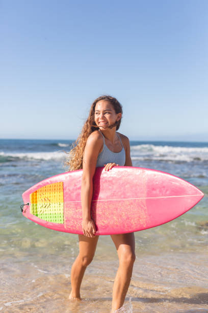 No school, it's surfing time! An adolescent girl walks out of the water with a big smile and a surfboard under her arm. It's a sunny day and the waves look perfect! body board stock pictures, royalty-free photos & images