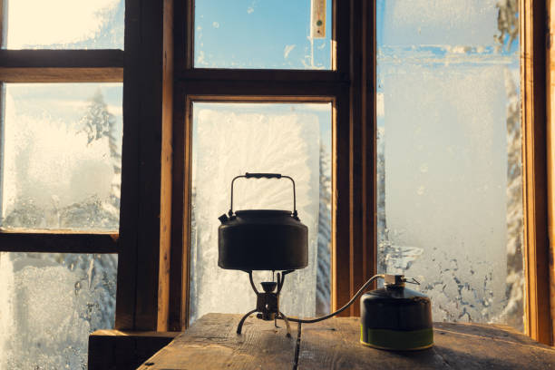 small kettle stands on a gas burner against a window in a frost - home interior cabin shack european alps imagens e fotografias de stock