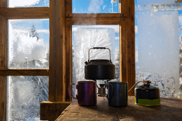 small kettle stands on a gas burner next to steel cups - home interior cabin shack european alps imagens e fotografias de stock
