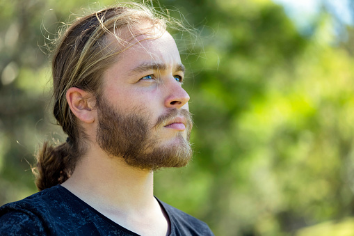 Portrait of young man with ponytail, background with copy space, full frame horizontal composition