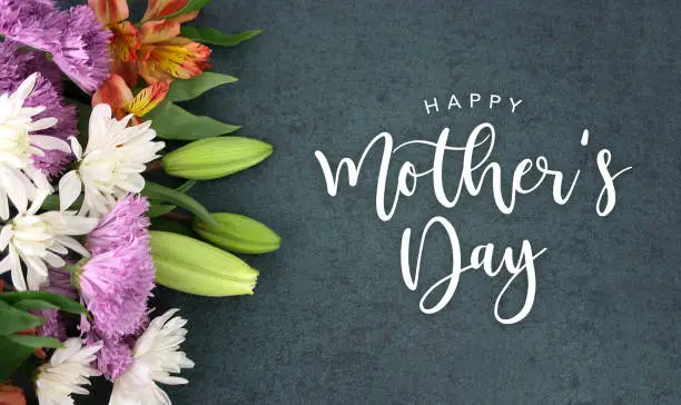 Photo of Happy Mother's Day calligraphy holiday script over dark blackboard background with beautiful colorful white, pink, orange, purple and green flower blossom bouquet