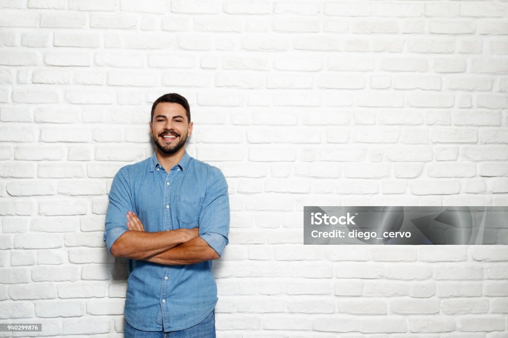 Facial Expressions Of Young Beard Man On Brick Wall Portrait of happy Italian man smiling against white wall as background and looking at camera. Men Stock Photo