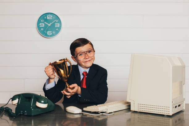 Young Retro Business Boy in Office with Trophy A young business boy dressed in business suit and tie sits at his office desk holding his winning trophy. He is super hard worker and has recently won every competition in company performance. retro salesman stock pictures, royalty-free photos & images