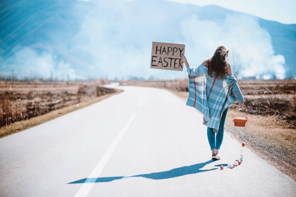 istock Sensual Female on Empty Road Hitchhiking with Raised Happy Easter Board 940334554