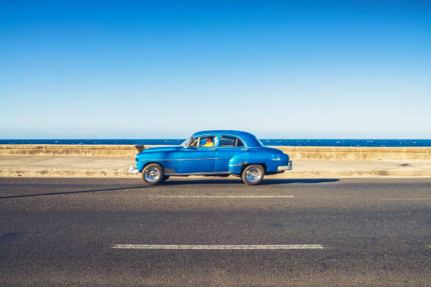 Vintage car driving along coast,with the Caribbean Sea in the background, The Malecon, Havana Centro, Cuba.