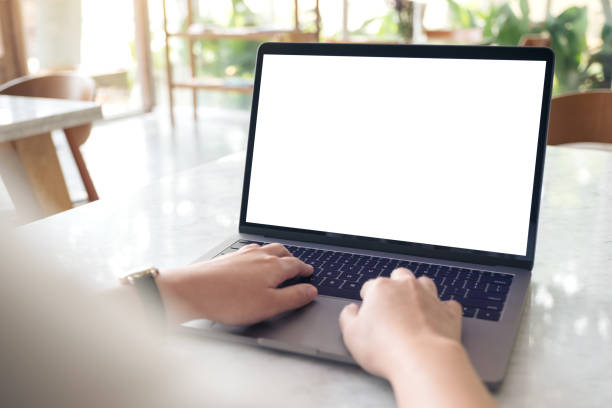 istock Mockup image of hands using and typing on laptop with blank white desktop screen on table in modern cafe 940348442