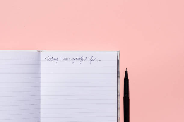 Gratitude journal and pen on pink background from above