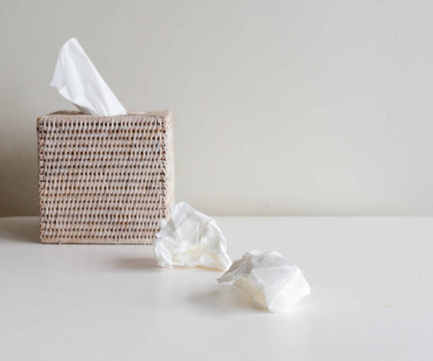 Tissue box and crumpled tissues on white table Rattan tissue box and crumpled tissues on table - cold and flu season concept, grief concept (selective focus) facial tissue stock pictures, royalty-free photos & images