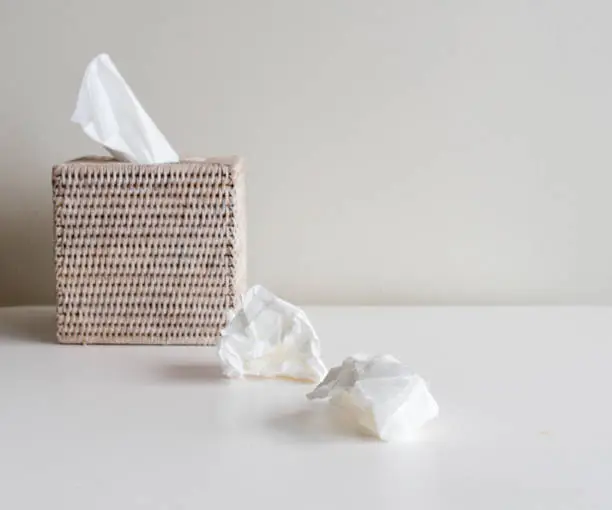 Rattan tissue box and crumpled tissues on table - cold and flu season concept, grief concept (selective focus)