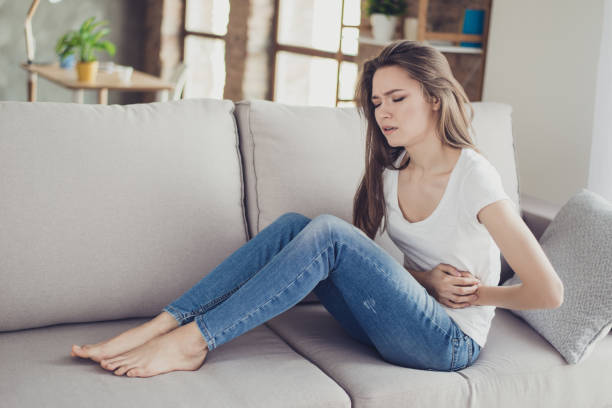 Sad beautiful woman sitting on the couch and feeling spasm and symptoms of pms Sad beautiful woman sitting on the couch and feeling spasm and symptoms of pms pms photos stock pictures, royalty-free photos & images