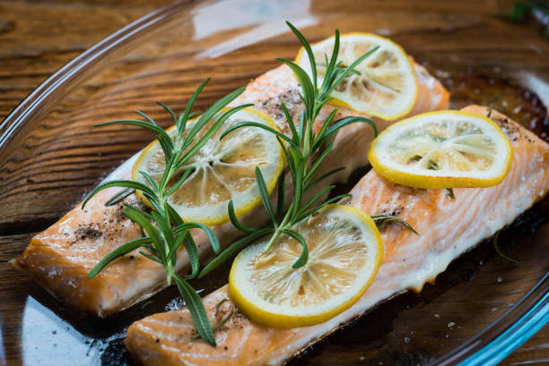 istock Salmon. Two juicy salmon steaks in roast pan with herb decoration on rustic oak table. 940374462