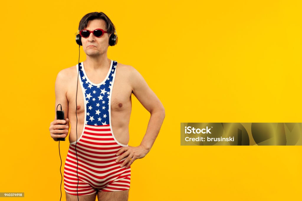 studio portrait of a mature man studio portrait of a mature man in a beach swimsuit with a mobile phone on a yellow background Bizarre Stock Photo