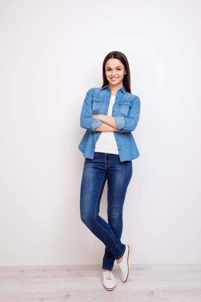 Pretty young woman in jeans and shirt standing with crossed hands against white background Pretty young woman in jeans and shirt standing with crossed hands against white background women young women standing full length stock pictures, royalty-free photos & images