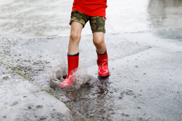 istock Child wearing red rain boots jumping into a puddle. 940381464