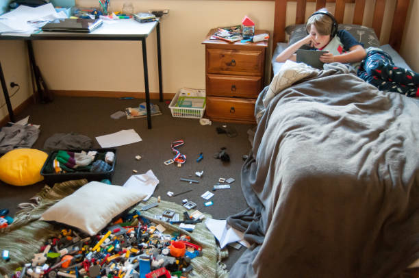Child laying in bed on electronic device with a very messy room