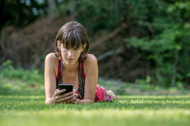 istock Adult woman laying on grass using digital reader 940415228