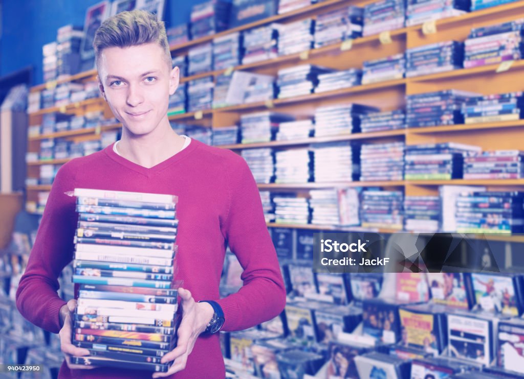 Portrait of smiling young male holding stack of DVDs Portrait of smiling young male holding stack of DVDs in shop indoors DVD Stock Photo