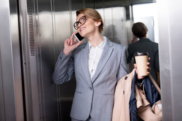 istock smiling businesswoman in suit talking on smartphone in elevator 940424068