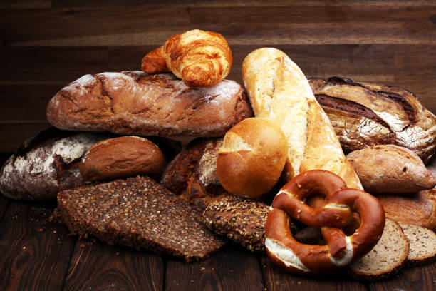 istock Different kinds of bread and bread rolls on board from above. Kitchen or bakery poster design 940429192