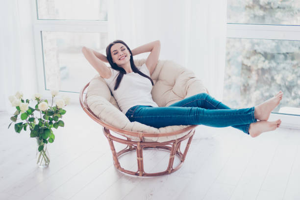 istock Cheerful young cute pretty woman enjoying  weekend while sitting on comfort soft modern armchair with white rose at home 940441872