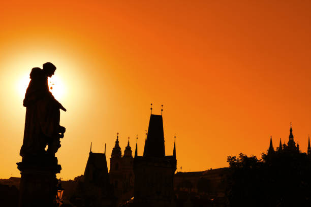 Sunset backlit silhouettes of statues and roofs of cityscape skyline at Charles Bridge in Prague, Czech Republic