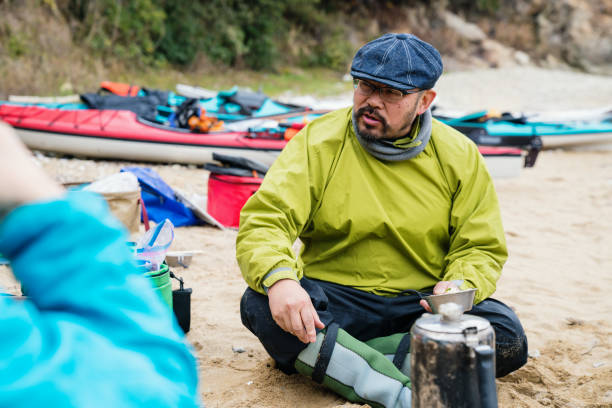 A man eating lunch on a beach with sea kayaks in the back
