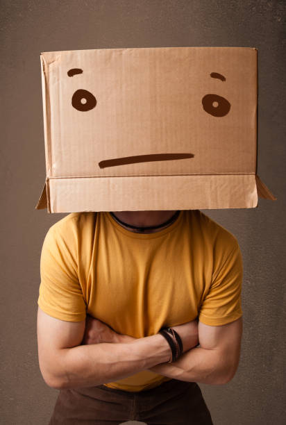 istock Young man gesturing with a cardboard box on his head with straight face 940449410