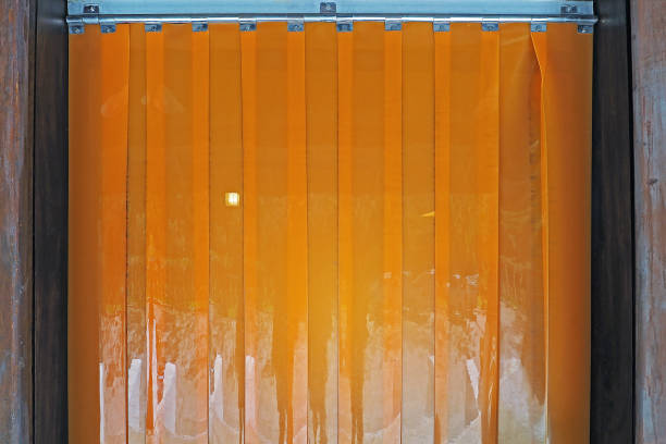 orange color Industrial warehouse plastic PVC strip curtains hanging at the wood door stock photo