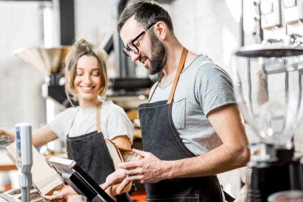 Coffee sellers working in the shop Two sellers in uniform filling bags with coffee beans working in the coffee store market vendor stock pictures, royalty-free photos & images