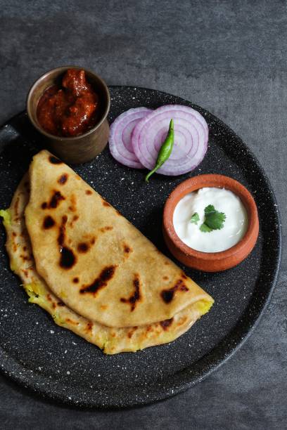 istock Aloo Paratha - Indian potato stuffed wheat bread served with Raita and mango pickle on dark moody background, Top down view 940455514