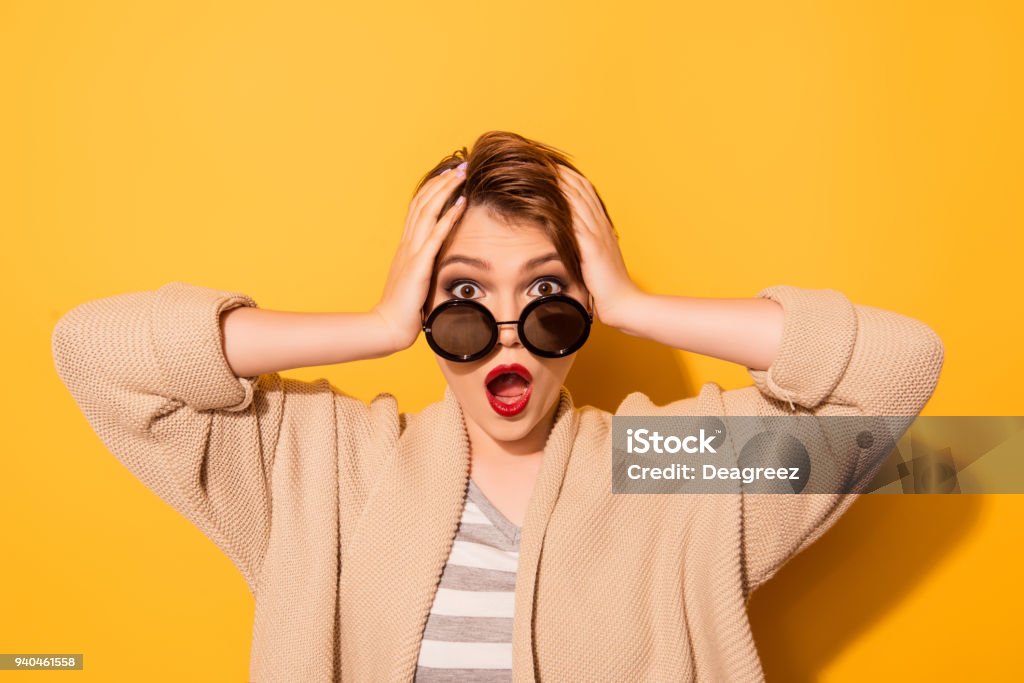 No way! Close up portrait of shocked girl in stylish sunglasses and casual wear on the yellow background Awe Stock Photo