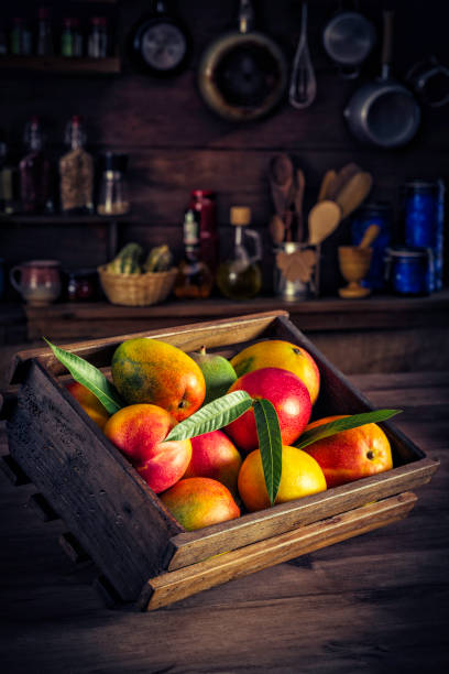 istock Tropical fruits: Wooden crate with assorted mangos in rustic kitchen. Natural lighting 940469156