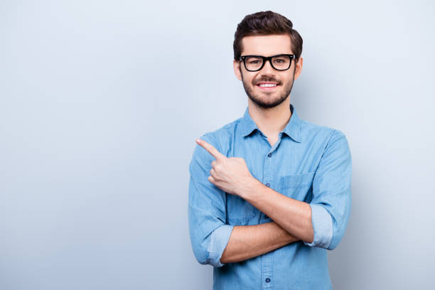 joyeuse beau jeune homme j’ai des lunettes est indiquant la direction et en pointant avec son doigt - man pointing photos et images de collection