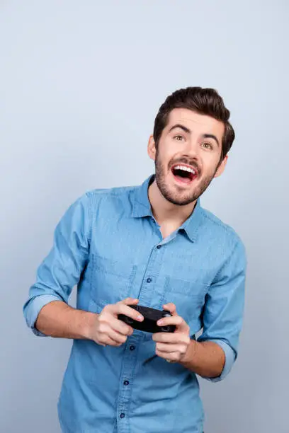 Portrait of young man holding joystick and playing videogames. He is very excited