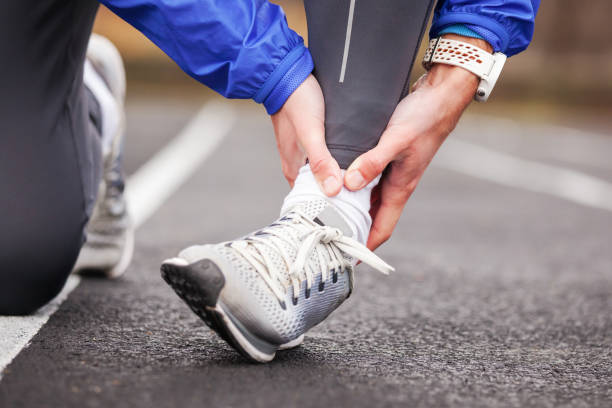 colpo ritagliato di un giovane che tiene la caviglia nel dolore sloga un piede. - ankle foto e immagini stock